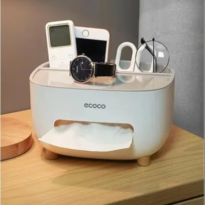 Hand pulling a paper tissue from a white Ecoco Tissue Box with small wooden legs on a wooden table.
