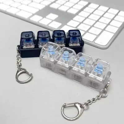 Black and clear mechanical keyboard keychain fidget toys displayed next to a white computer keyboard on a desk.
