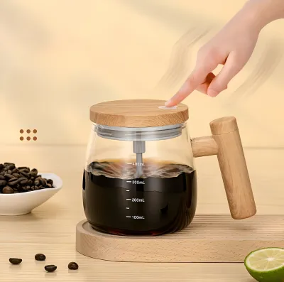 Hand pressing the button on top of a self stirring glass mug containing hot black coffee on a tray