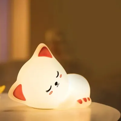 Close-up of the silicone cat night lamp emitting a soft warm light in a dimly lit bedroom setting.