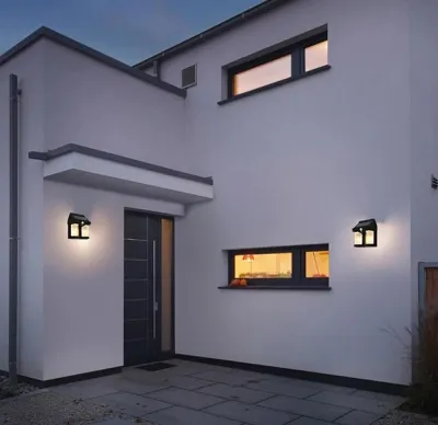 Two Solar Wall Lights installed on a modern white house exterior wall glowing with warm illumination at night.